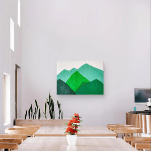 Green mountain landscape painting displayed in a bright cafe with wooden furniture.