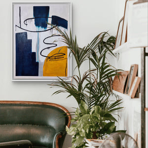 Abstract handmade painting with vibrant blue and yellow tones displayed in a cozy lounge with plants.
