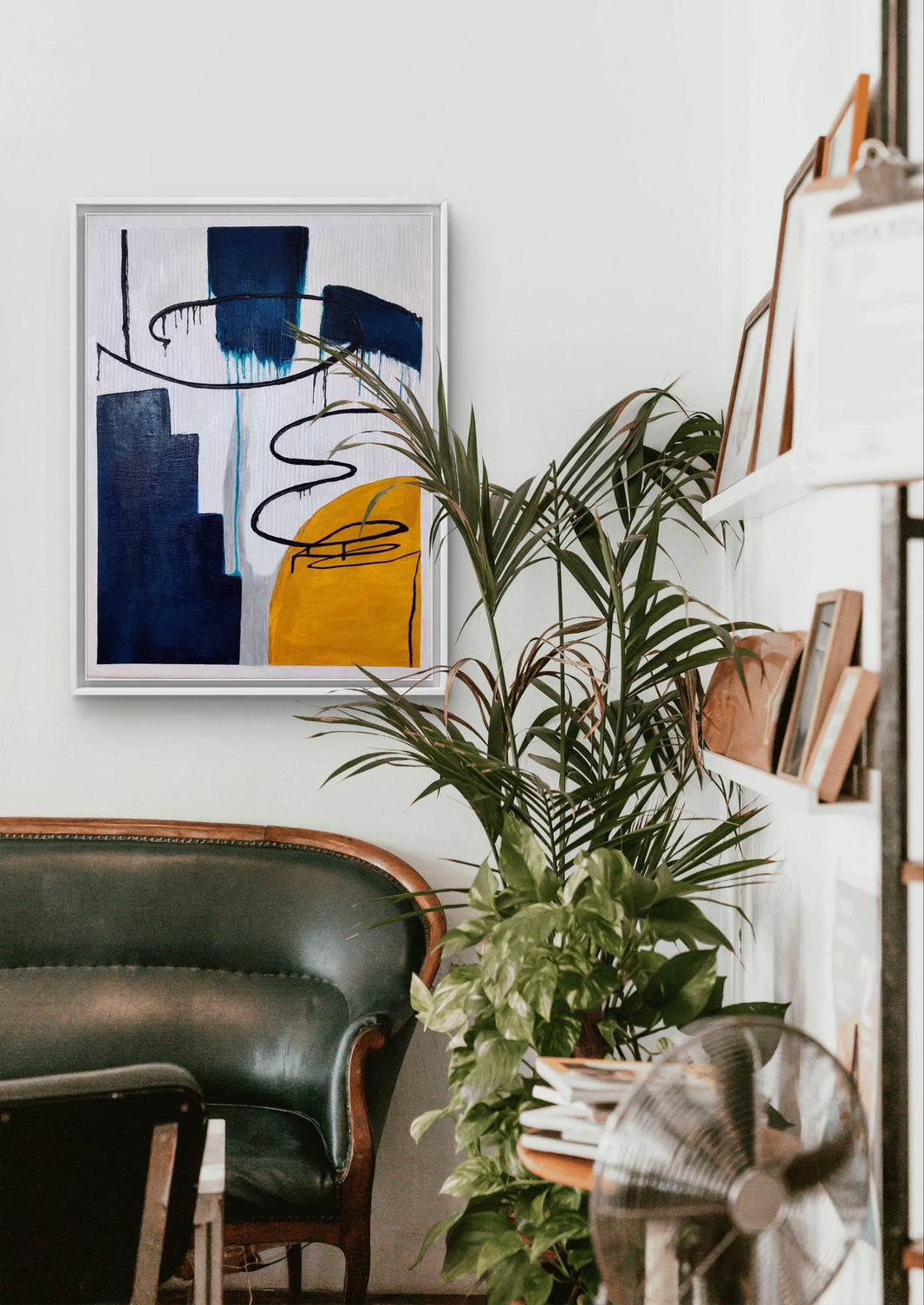 Abstract handmade painting with vibrant blue and yellow tones displayed in a cozy lounge with plants.