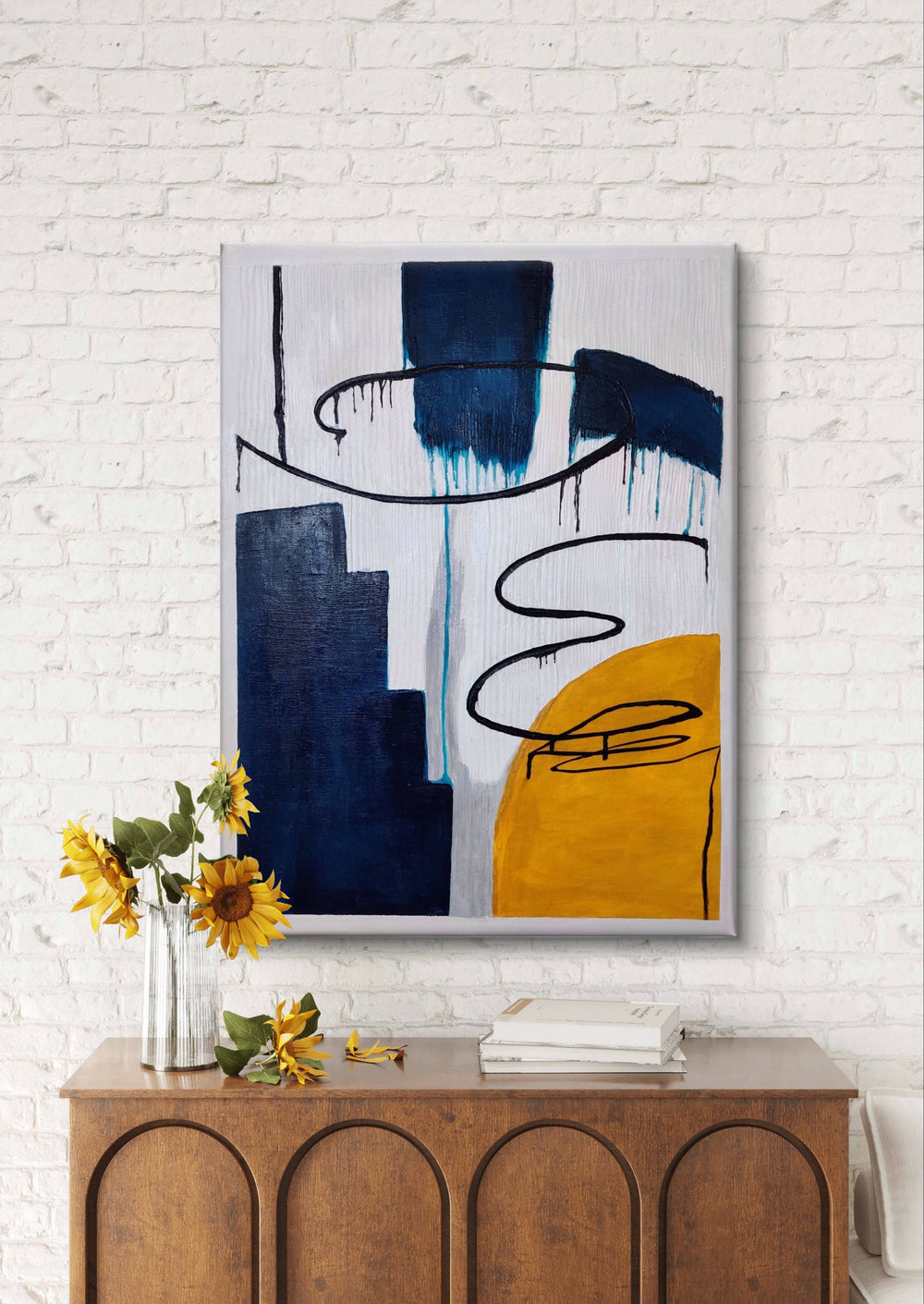 Handmade abstract painting with bold colors displayed on a white brick wall above a wooden console.