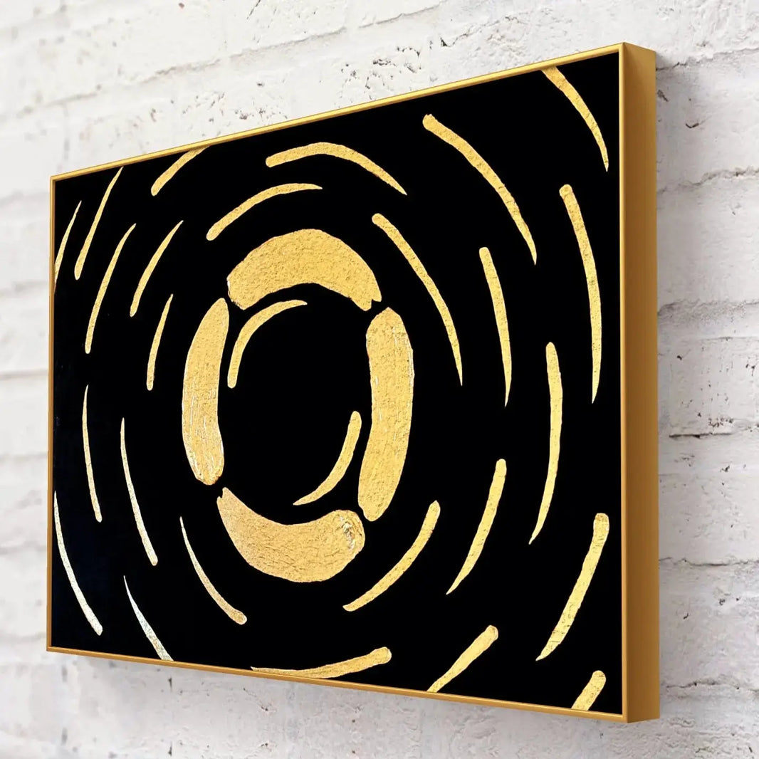 Close-up side view of a gold and black abstract textured painting with a golden frame against a white brick wall.